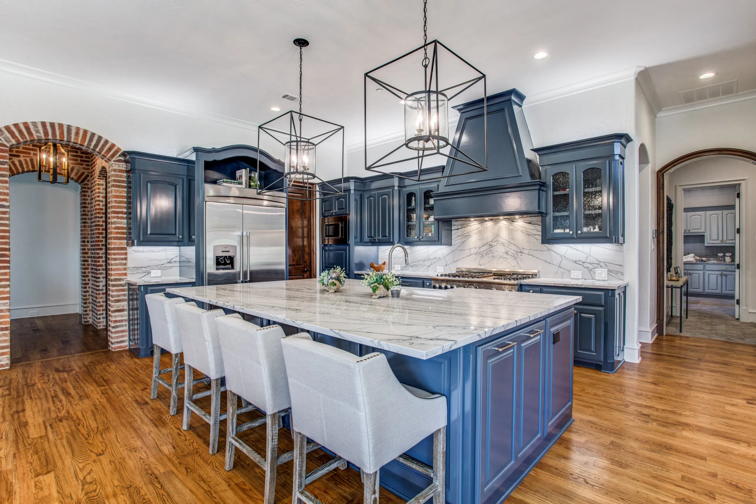 A grand open great room with wood-beam ceilings opening to a white chef’s kitchen.