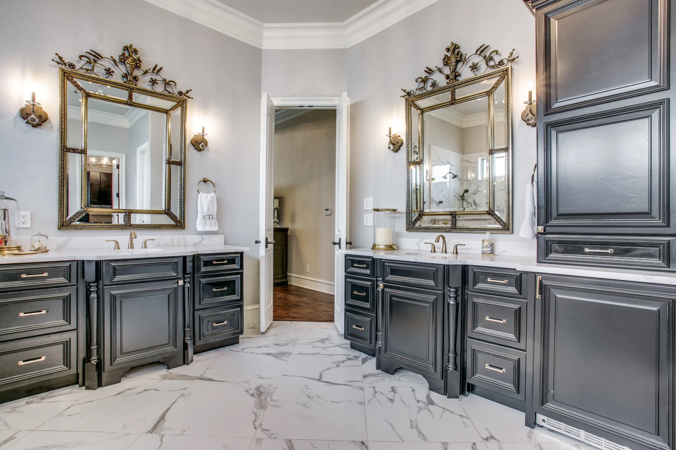 A spa-grade primary bath with dual gilt-framed mirrors, marble floors, and furniture-style vanities.