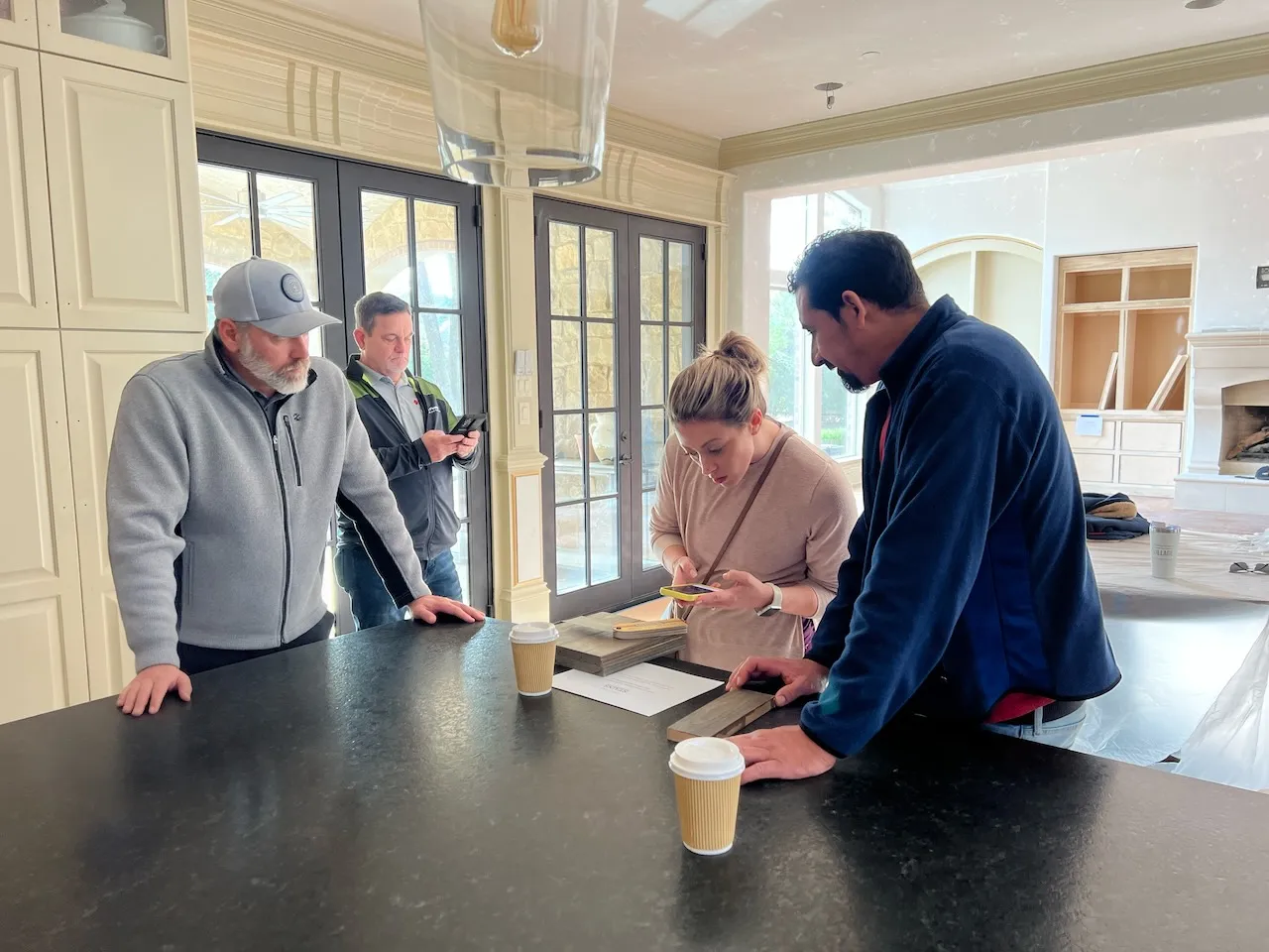 Chad Swanson meeting with a homeowner and her interior designer in the kitchen of an active Southlake renovation — reviewing material samples on the island.