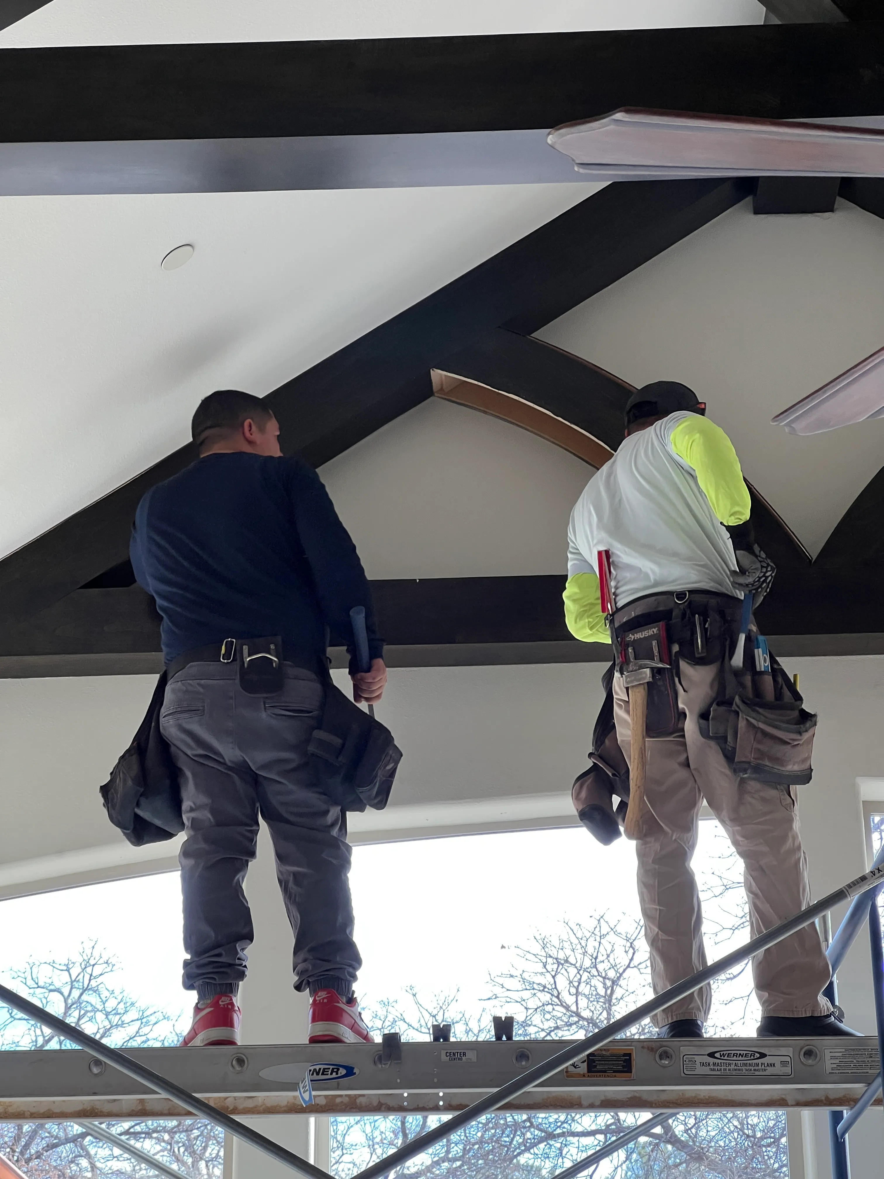 Swanson crew members on scaffold finishing a black beam mid-project.