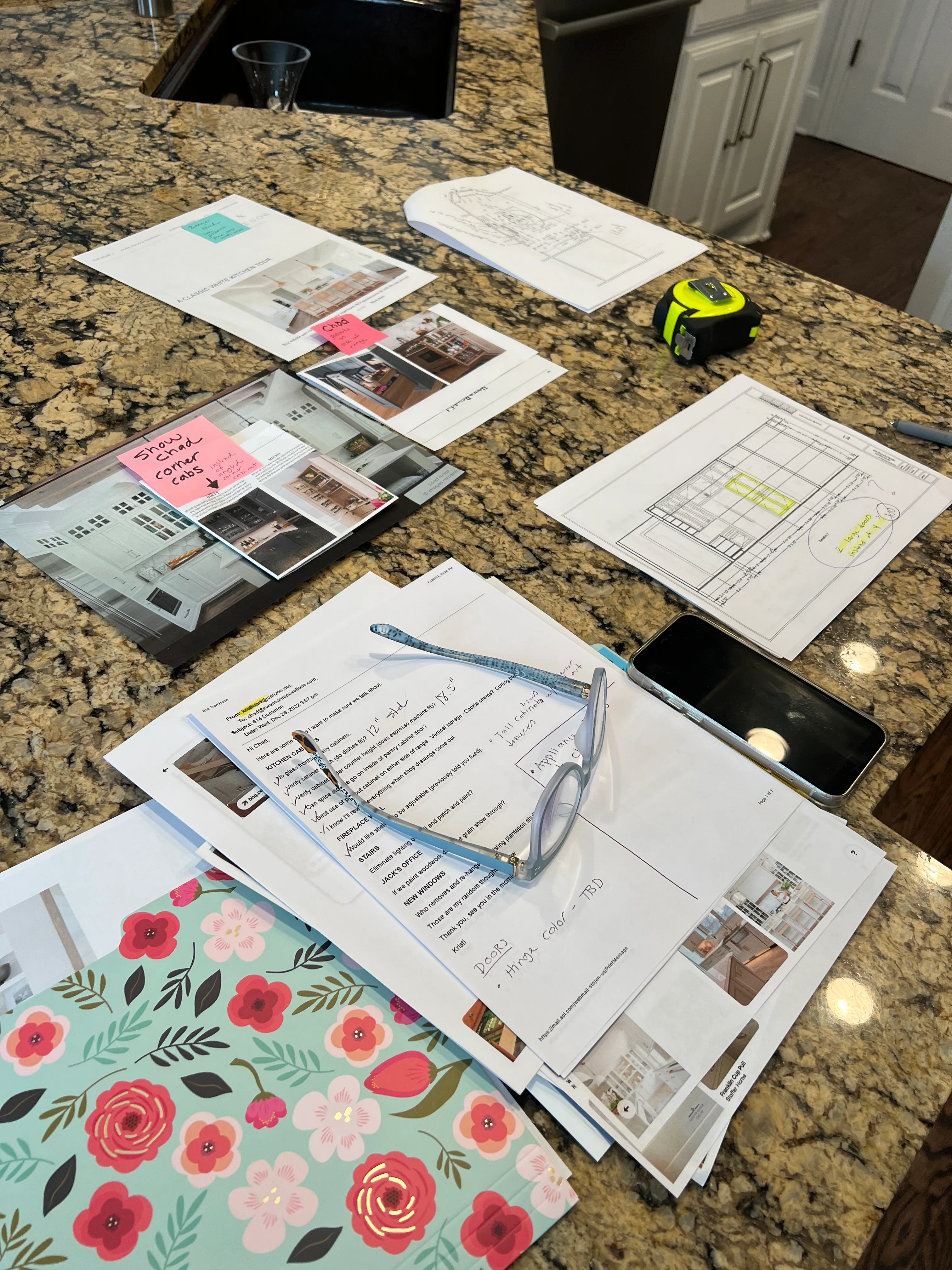 Materials palette on a Southlake kitchen island — tile samples, hardware pulls, sketches, and post-it notes marked 'show Chad corner cabs.'