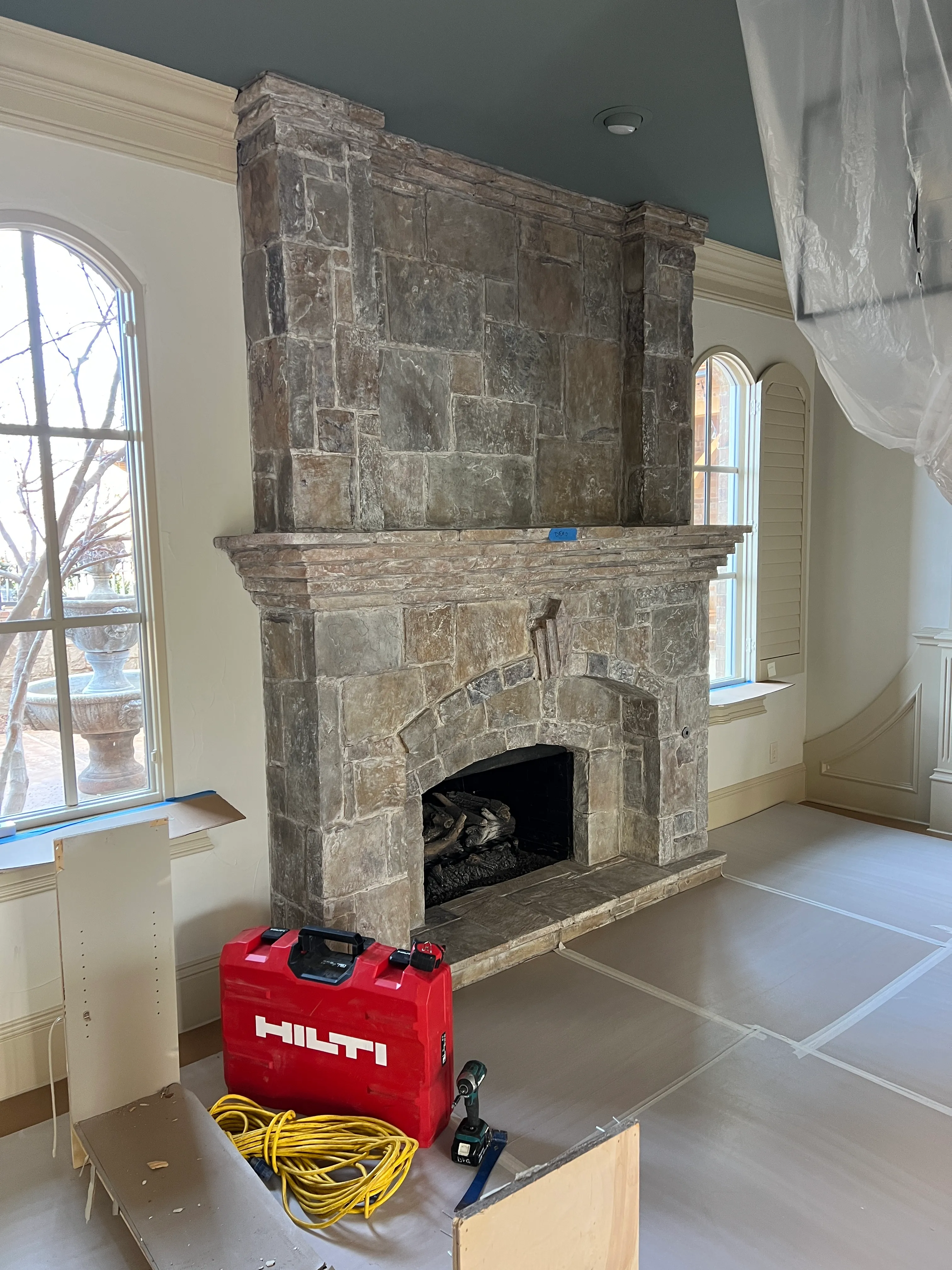 A stone chimney breast wrapped in plastic protection during adjacent trades' work — Swanson's finished-area barrier standard.