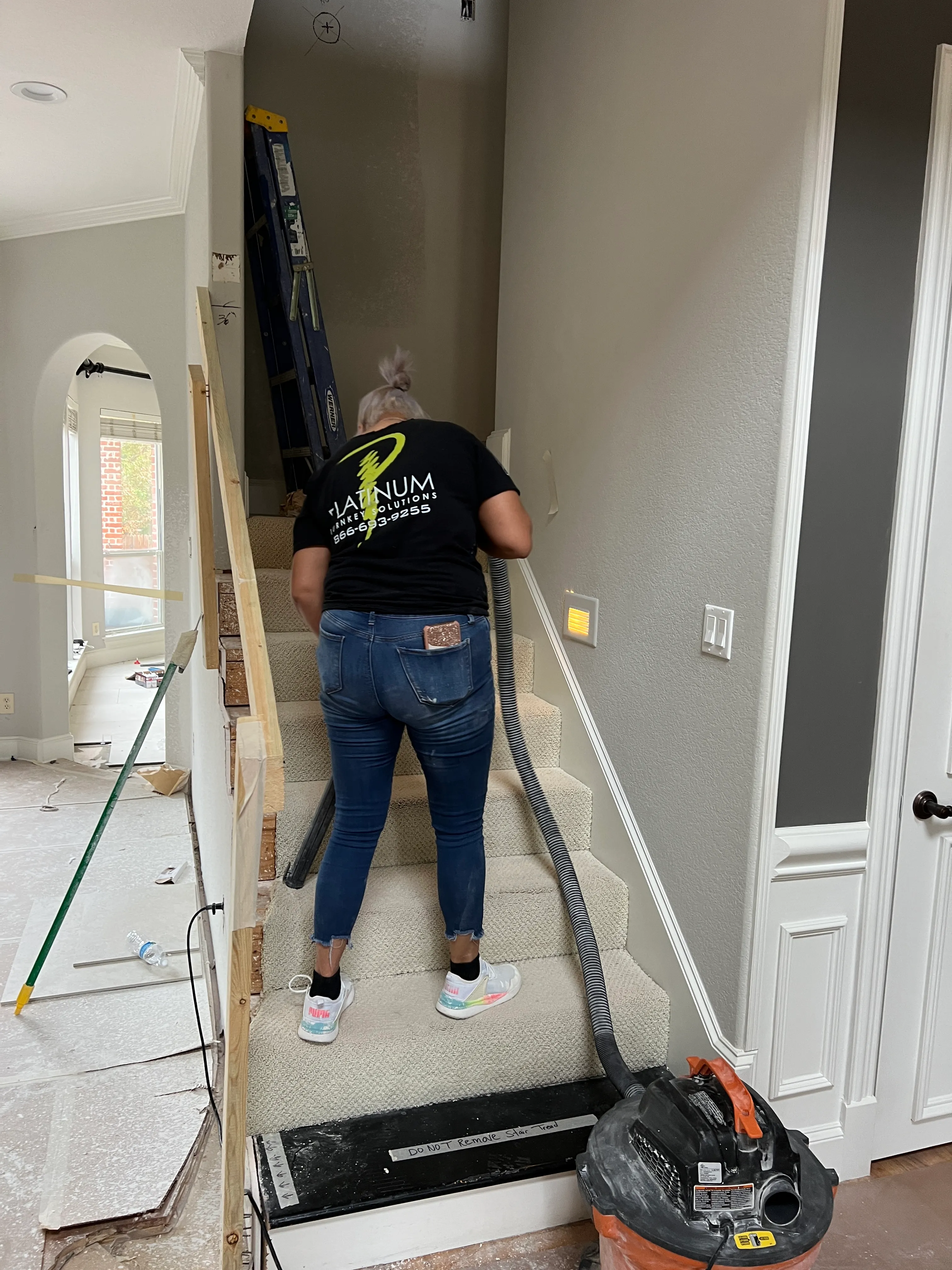 Dust-control specialist vacuuming a covered staircase mid-project — negative-air and HEPA vacuum treatment daily.